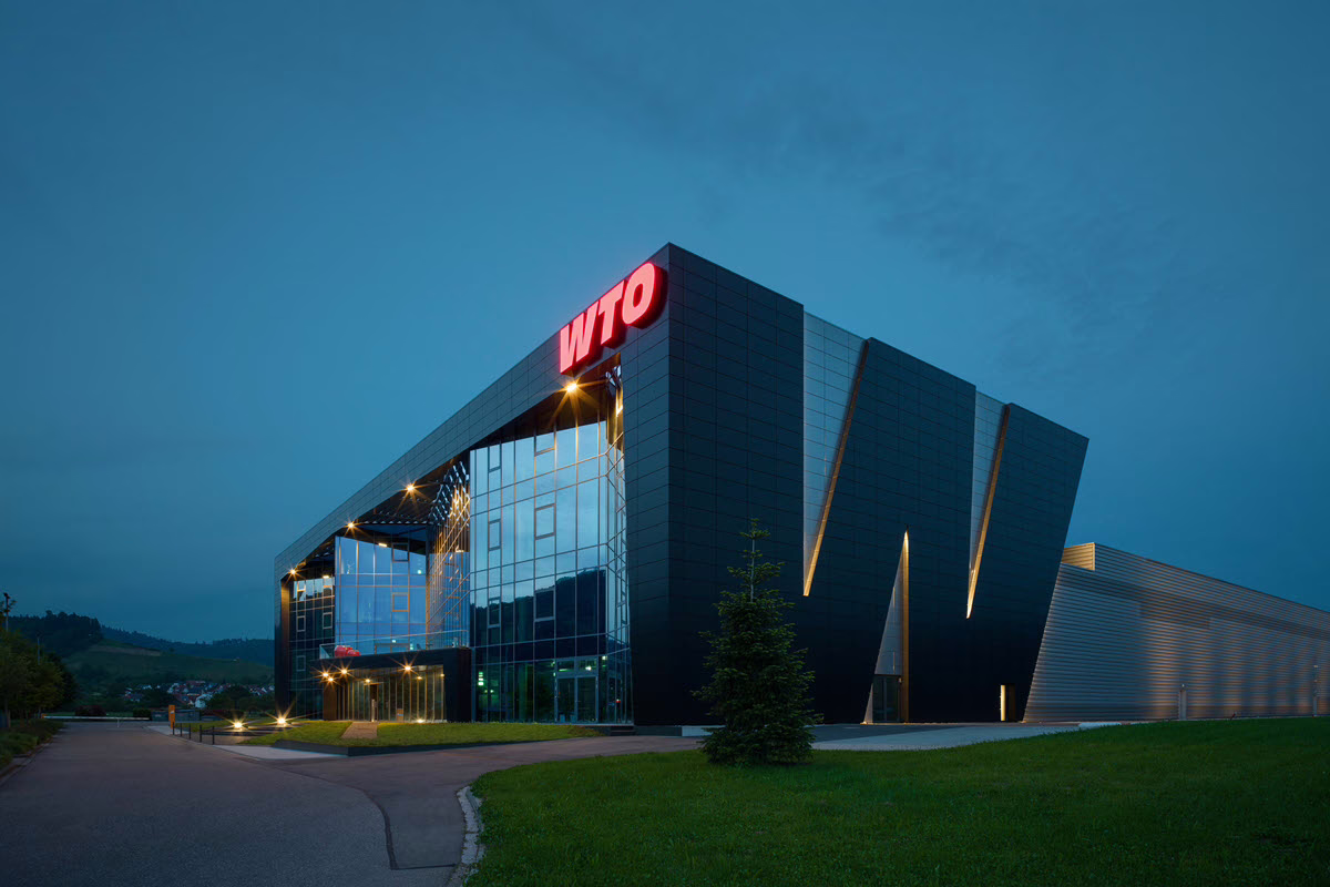 Firmengebäude mit beleuchtetem WTO-Schriftzug in der Abenddämmerung.